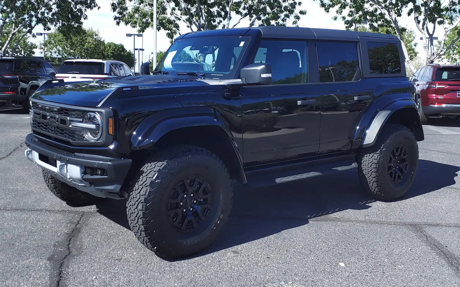 Ford Bronco Raptor negro de cuatro puertas, generación U725, en tres cuartos frontal izquierdo en el patio de un concesionario. Se distinguen la parrilla con letras FORD y luces ámbar de marcación, los guardafangos ensanchados con tornillería expuesta y las llantas todoterreno de 37" sobre rines negros. Imagen referencial del modelo, no de la unidad en venta.