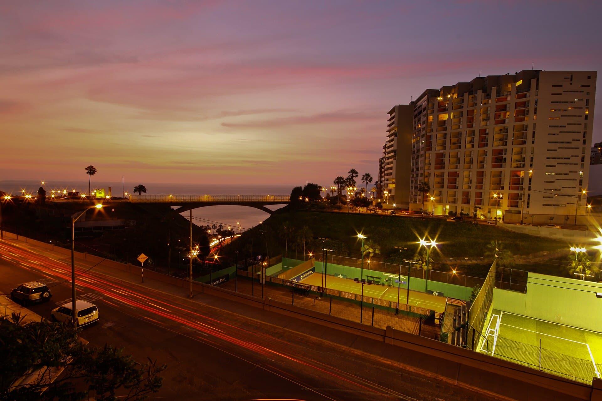 Avenida de Miraflores, Lima, al atardecer con luces de autos en movimiento y el mar al fondo