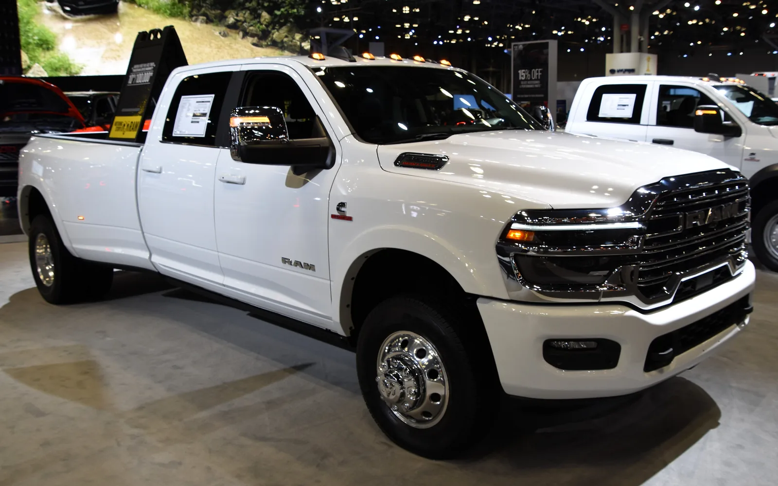 RAM 3500 Limited Longhorn Crew Cab blanca, quinta generación DT, con caja larga y rueda trasera doble (dually), en tres cuartos frontal derecho sobre el piso de un salón del automóvil. Se distinguen la parrilla cromada con letras RAM, las cinco luces ámbar de gálibo sobre el parabrisas y la toma de aire elevada del capó. Imagen referencial del modelo, no de la unidad en venta.