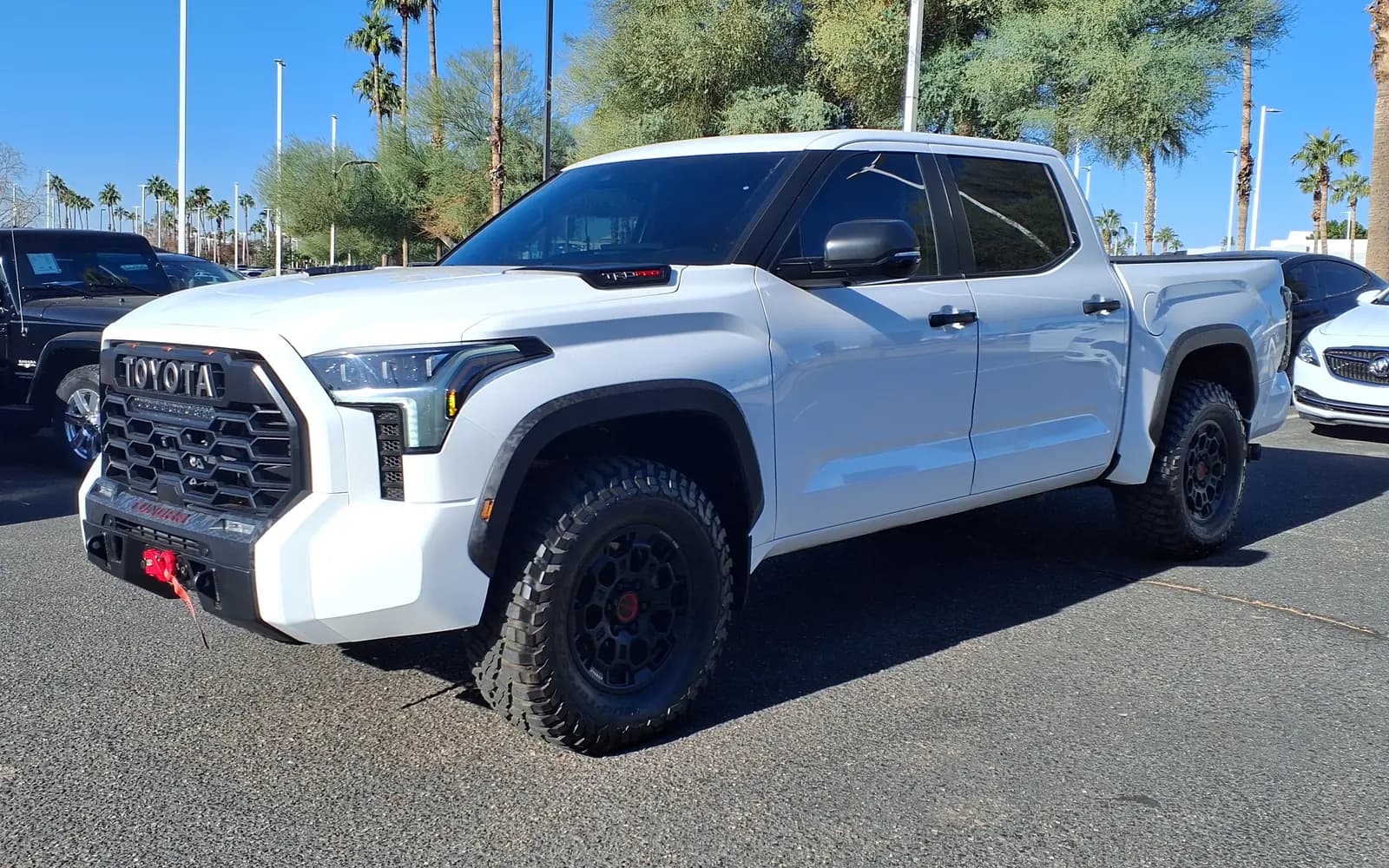 Toyota Tundra TRD Pro blanca, generación XK70 con cabina CrewMax de cuatro puertas, en tres cuartos frontal izquierdo en el patio de un concesionario. Se distinguen la parrilla heritage con TOYOTA en letras de bloque, la toma de aire TRD PRO del capó, el gancho de rescate rojo y los rines negros con tapa central roja. Imagen referencial del modelo, no de la unidad en venta.